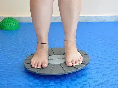 A woman stands barefoot with both feet on a round balance board