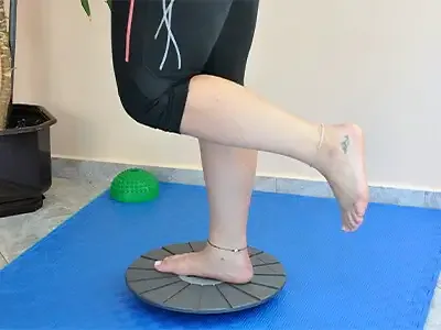 A woman stands on one leg on the balance board with the other leg bent back