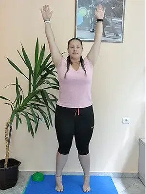 A woman stands on her toes with her arms raised high