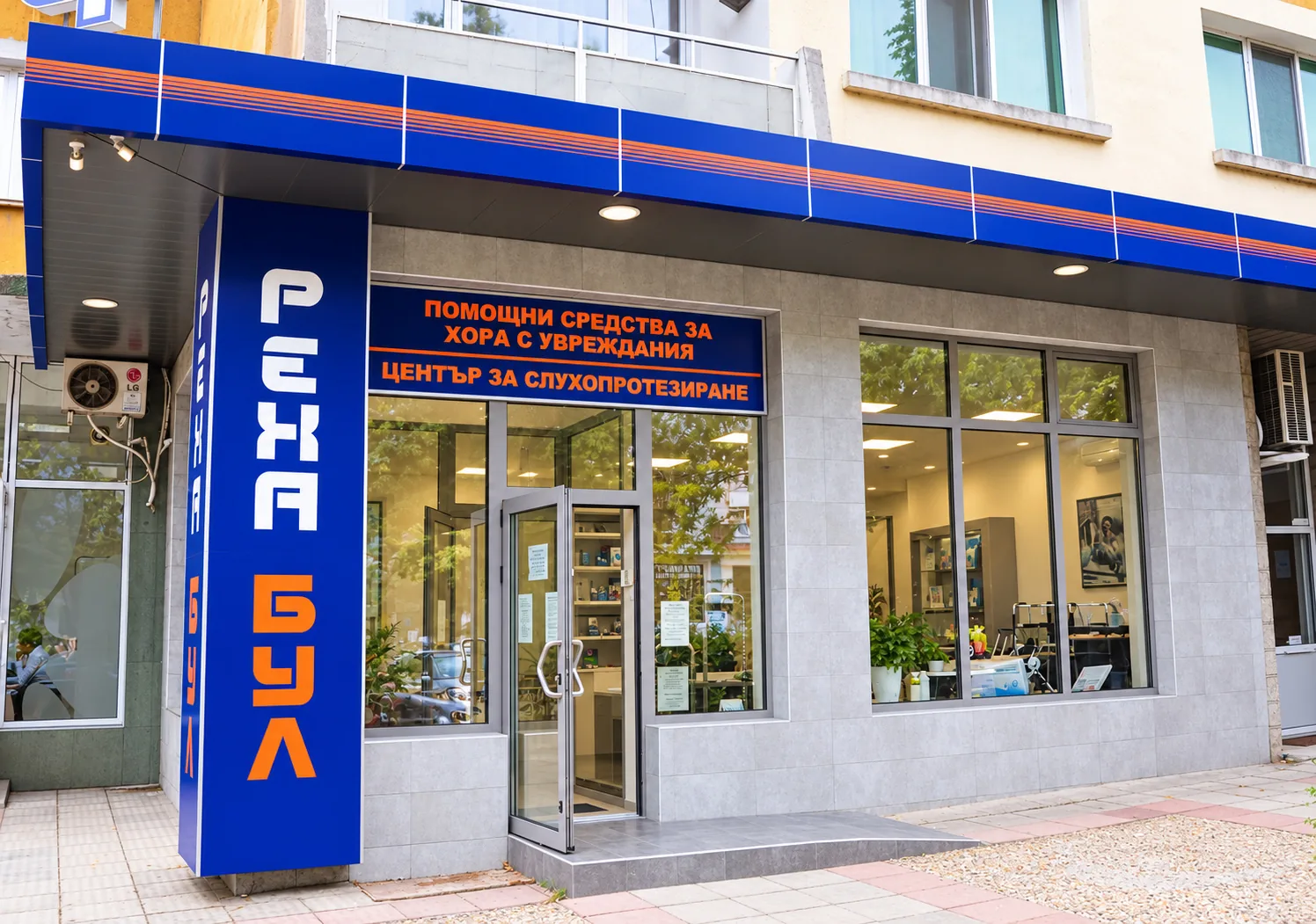The Reha Bul shop in Stara Zagora from outside: a blue sign that reads “Assistive devices for people with disabilities, hearing aid centre” in Bulgarian, tall “Reha Bul” lettering and a ramp to the entrance